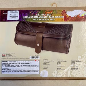 May include: A brown leather bike tool bag kit. The bag features a woven design on the flap and a strap closure. The box reads "BIKE TOOL BAG" in English, Spanish, and French.