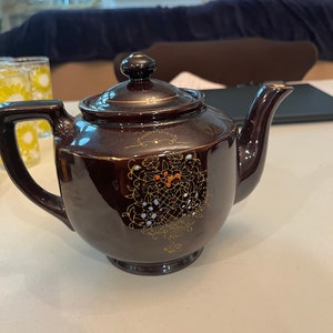 May include: A brown teapot with gold and white floral designs. The teapot has a lid and a spout.