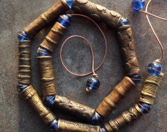 May include: A necklace made of brass and blue glass beads. The brass beads are cylindrical and have a textured surface. The blue glass beads are round and have a shiny finish.