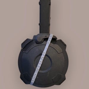 Puede incluir: Un objeto cilíndrico negro con un asa y una base circular. Una correa gris claro con el texto "D60 STRAP ZEN" está envuelta alrededor del objeto. El objeto tiene un acabado mate sobre un fondo neutro.