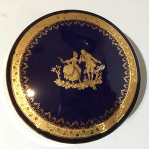 Puede incluir: Un plato decorativo redondo azul marino con un borde dorado y un borde de filigrana dorada. El centro presenta una ilustración dorada de una pareja con ropa de época. Una pieza clásica para exhibir.