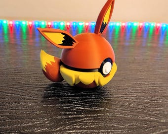 May include: A 3D printed figurine of a red and yellow Pokemon character, resembling a fox with a large, round head and a white eye.