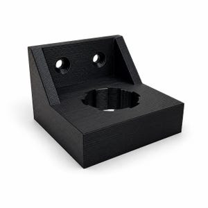 May include: A black 3D-printed L-shaped mounting bracket featuring a flat base with a central circular opening and a vertical back panel containing two countersunk screw holes. The surface exhibits a fine, layered texture from the printing process.