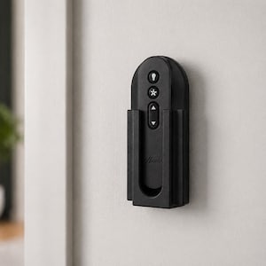 May include: A black wall-mounted remote control for a ceiling fan, featuring a rounded top and a rectangular cradle. The remote has three buttons with white icons for light, fan speed, and direction, with the Hunter brand name embossed below.