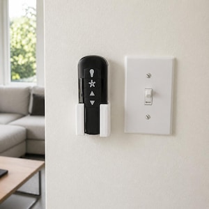 May include: A black ceiling fan remote control with white icons for light, fan speed, and direction, housed in a white wall-mounted holder next to a standard white rectangular light switch plate with a single toggle switch on a white wall.