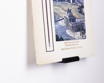 May include: A black vinyl record holder with a record featuring an aerial view of the Brandenburg Gate in Berlin, Germany. The record cover text reads "Jean-Francois Paillard Chamber Orchestra Jean-Francois Paillard, Director".
