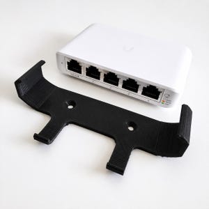 May include: A white network switch with five Ethernet ports labeled PoE IN and 1 through 5, alongside a black 3D-printed mounting bracket featuring two circular screw holes and four curved arms designed to hold the device securely in place.