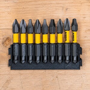 Op de afbeelding: Een set van negen DeWalt-schroefbits met zwarte punten en gele schachten, georganiseerd in een zwarte kunststof houder. Elke bit heeft de merknaam DeWalt op het gele gedeelte gedrukt, met verschillende puntvormen zichtbaar in de rij.