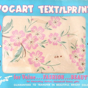May include: A pack of iron-on transfer patterns featuring a floral design with pink flowers and green leaves. The pack is blue and white and says "Vogart Text/Lprints" and "for Value... FASHION... BEAUTY!"  The text also says "Guaranteed to transfer in beautiful bright colours".