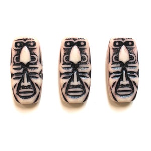 May include: Three white ceramic beads with black tribal face designs. The beads are rectangular in shape and have a smooth, glossy finish.