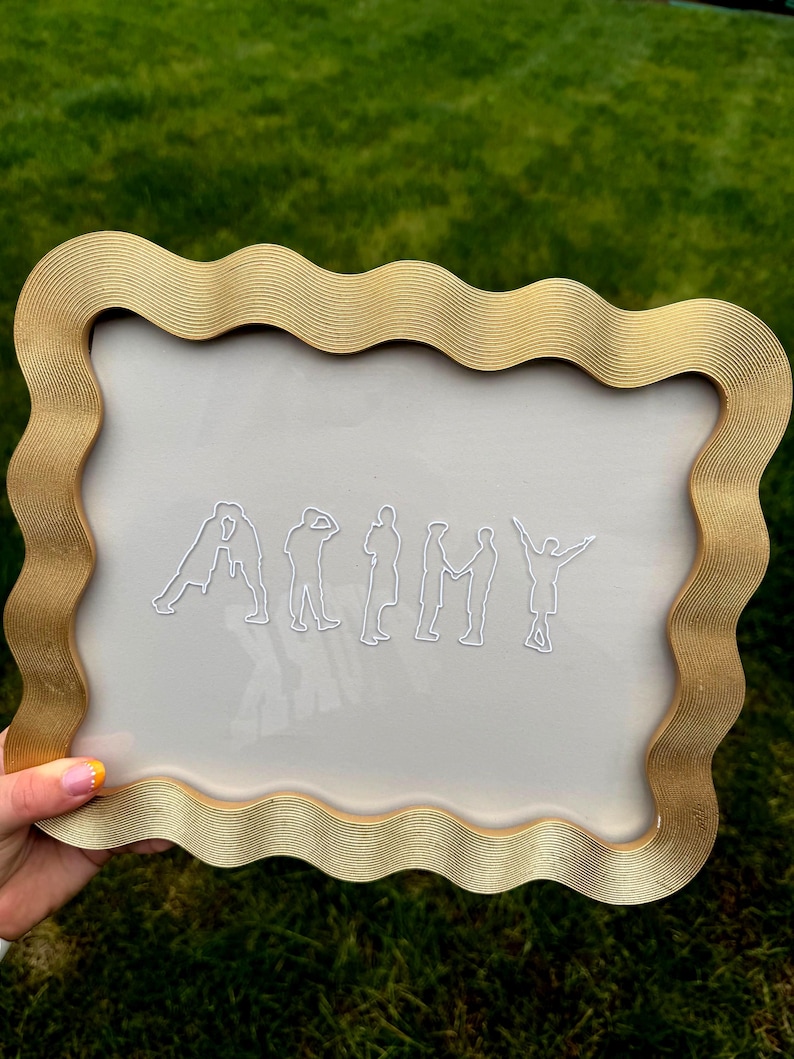 Puede incluir: Un marco rectangular con un borde dorado ondulado que rodea un panel transparente. El centro presenta siluetas de l&iacute;neas blancas de siete figuras dispuestas para deletrear la palabra ARMY, donde cada figura representa una letra.
