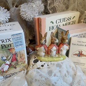 May include: A collection of Beatrix Potter themed items, including a Beswick box, small books, and a figurine of three rabbits wearing red capes. The books include "Guess How Much I Love You" and "The Tale of the Flopsy Bunnies."