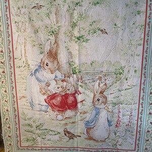 May include: A fabric panel featuring a watercolor illustration of rabbits in a forest setting. The rabbits are dressed in blue and red jackets. The border has a floral design in red and green.