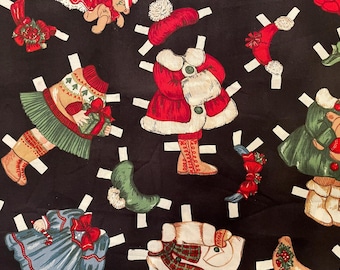 May include: A black fabric featuring colorful Christmas-themed paper dolls. The dolls are dressed in festive outfits, including red coats, green skirts, and hats. The design includes paper doll cutouts with white tabs, creating a playful, holiday-themed pattern.