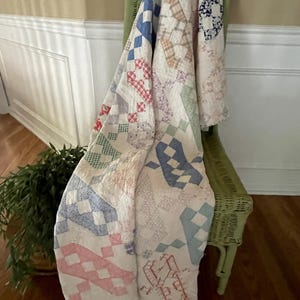 May include: A patchwork quilt featuring a white background with various geometric patterns in shades of blue, red, green, and pink. The quilt is constructed from multiple fabric squares and rectangles, showcasing a repeating block design throughout.