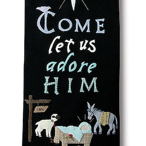 May include: A black fabric wall hanging with the text "Come let us adore HIM" and a nativity scene. The top and bottom edges have decorative borders with script that reads "The King of Angels" and "Christ The Lord".