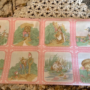 May include: A fabric panel featuring eight square illustrations of storybook animals in a garden setting. Each square has a pink border with a white floral design. The illustrations include rabbits, ducks, and other creatures.