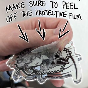 May include: A clear acrylic keychain featuring a black and white illustration of a character with spiky hair and a sword. The protective film is being peeled off the keychain. The text "FOR KEYCHAINZ! MAKE SURE TO PEEL OFF THE PROTECTIVE FILM" is written in black marker on a white background.