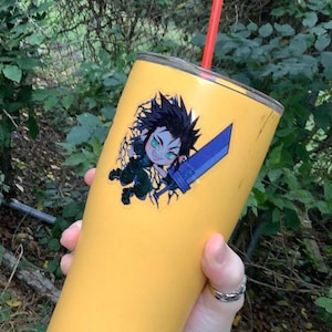 May include: A yellow stainless steel tumbler with a black and green anime character sticker. The tumbler has a red straw and the text "WELLNESS" on the bottom.