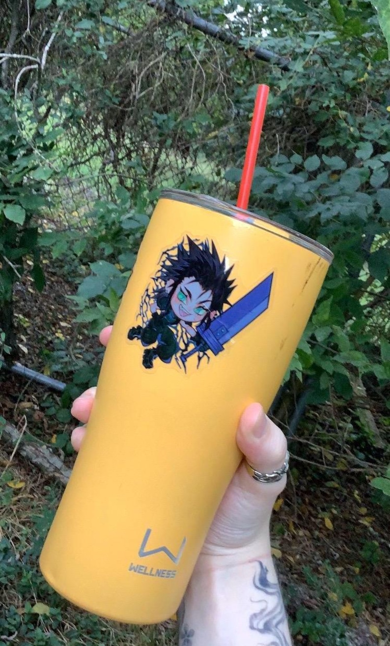 May include: A yellow stainless steel tumbler with a black and green anime character sticker. The tumbler has a red straw and the text "WELLNESS" on the bottom.
