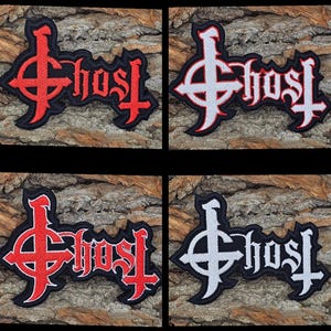 May include: Four embroidered patches featuring the word "Ghost" in a gothic font, with a symbol above the word. The patches are in red and black, and white and black color schemes. The patches are on a textured, brown background.