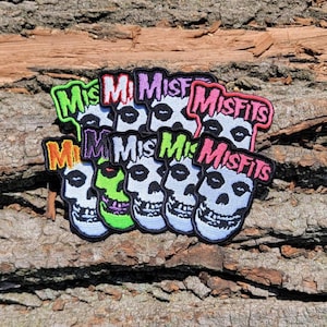 May include: A set of eight iron-on patches featuring a skull with a grinning mouth and the word "Misfits" in various colors, including pink, green, purple, and orange.