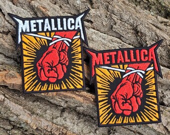 May include: Two black and yellow embroidered patches with the word "Metallica" in white lettering. Each patch features a red fist with white rope tied around it.