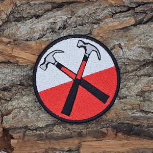 May include: A red and white circular patch with two crossed hammers, a black handle, and a silver head. The patch is embroidered with a design that resembles the album cover for "The Wall" by Pink Floyd.