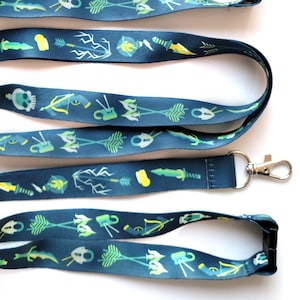 May include: Four blue lanyards with a repeating pattern of green, yellow, and white icons. The icons include arrows, swords, and other symbols. Each lanyard has a silver metal clip on one end and a black plastic clip on the other end.