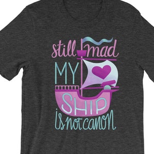 K&ouml;nnte beinhalten: Dunkelgraues Heather-T-Shirt mit dem Text "still mad my ship is not canon" in blauer und lila Schrift. Ein pinkfarbenes Schiff mit einem Herzsegel befindet sich in der Mitte des Textes.