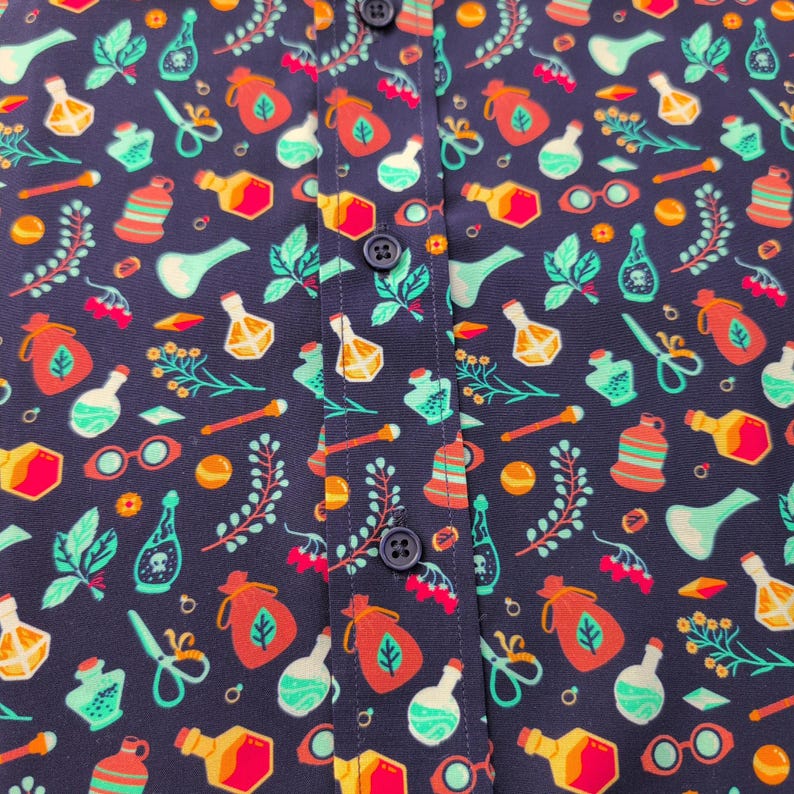 Puede incluir: Una camisa azul oscuro con botones y un patr&oacute;n colorido de frascos de pociones, bolsas y otros objetos m&aacute;gicos. La camisa tiene un cierre de botones y un cuello.