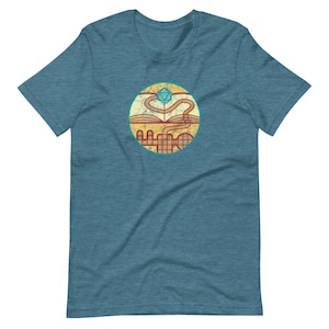 May include: A teal blue t-shirt with a circular graphic of a book with a winding path leading to a blue and green twenty-sided die.