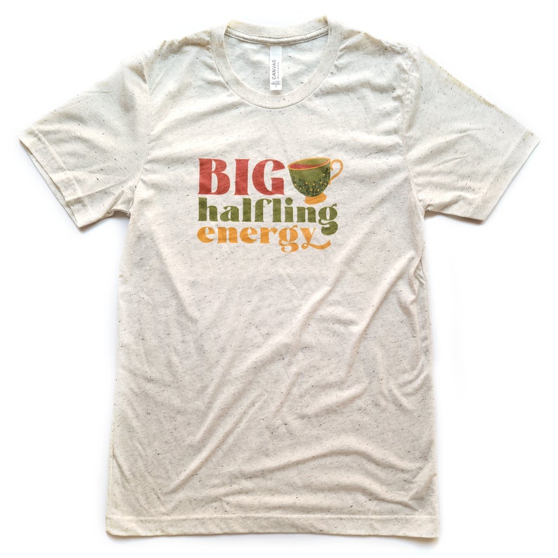 May include: A beige t-shirt with a graphic design that says "BIG halfling energy" with a green teacup illustration.