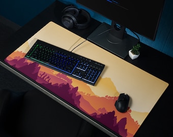 May include: A large rectangular mouse pad with a landscape design featuring a mountain range in shades of purple, orange, and yellow. A black keyboard, mouse, and monitor are on the desk. Headphones and a small plant are also visible.