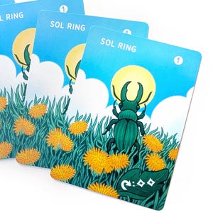 Puede incluir: Varias cartas de juego con un fondo de cielo azul, un sol amarillo y un escarabajo verde. Las cartas también presentan hierba verde, flores amarillas y el texto "SOL RING". Cada carta tiene un número en la esquina superior derecha.