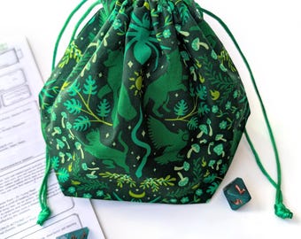 May include: Green drawstring bag with a forest-themed pattern featuring animals, plants, and mushrooms. The bag is made of fabric and has a green drawstring closure. Several teal dice are scattered around the bag.
