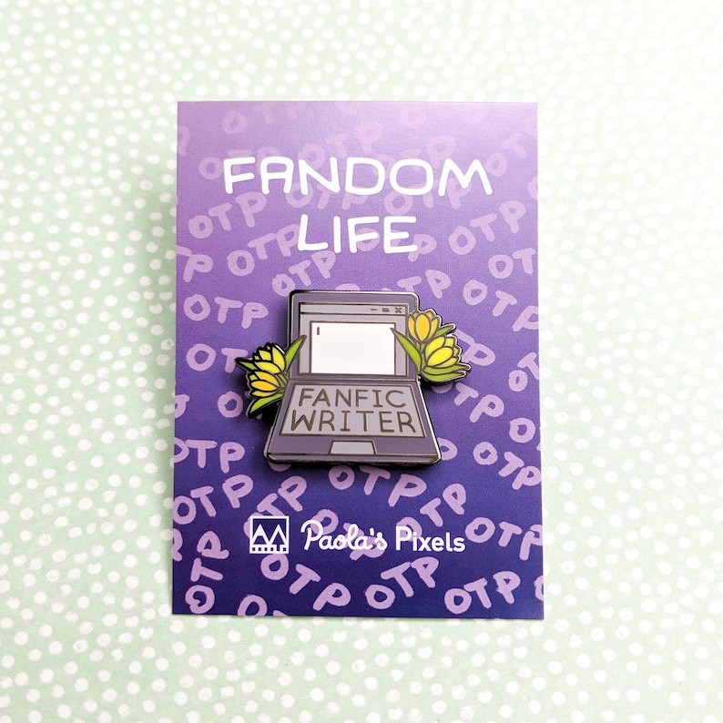 May include: A purple enamel pin with a laptop computer design. The laptop has the words "Fanfic Writer" on the screen. The laptop is surrounded by yellow flowers. The pin has the words "Fandom Life" and "Paola's Pixels" on it.