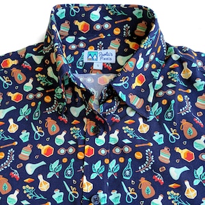 Puede incluir: Una camisa azul marino de botones con un patr&oacute;n caprichoso de frascos de pociones, hierbas y otros elementos m&aacute;gicos. La camisa tiene cuello y un frente abotonado. La etiqueta de la camisa dice "Paola's Pixels".