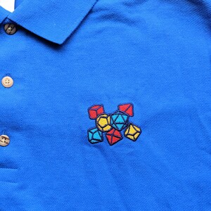 May include: A blue polo shirt with an embroidered design of colorful dice.