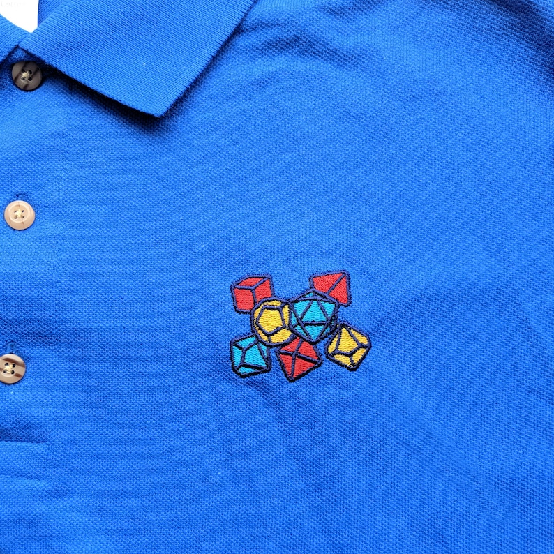 May include: A blue polo shirt with an embroidered design of colorful dice.