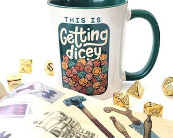 May include: A white ceramic mug with a green rim and handle. The mug has a graphic of dice and the text "This is Getting dicey".