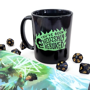 May include: Black coffee mug with a green and white graphic that says "You've Been Hellishly Rebuked". The mug is surrounded by black and gold dice.