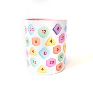 May include: A white ceramic mug with a pink rim, featuring a colorful pattern of geometric shapes with numbers printed on them. The numbers include 0, 4, 6, 8, 12, and 20.