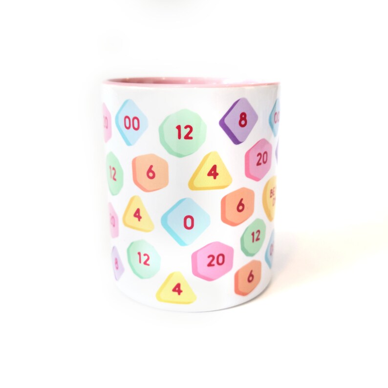 May include: A white ceramic mug with a pink rim, featuring a colorful pattern of geometric shapes with numbers printed on them. The numbers include 0, 4, 6, 8, 12, and 20.