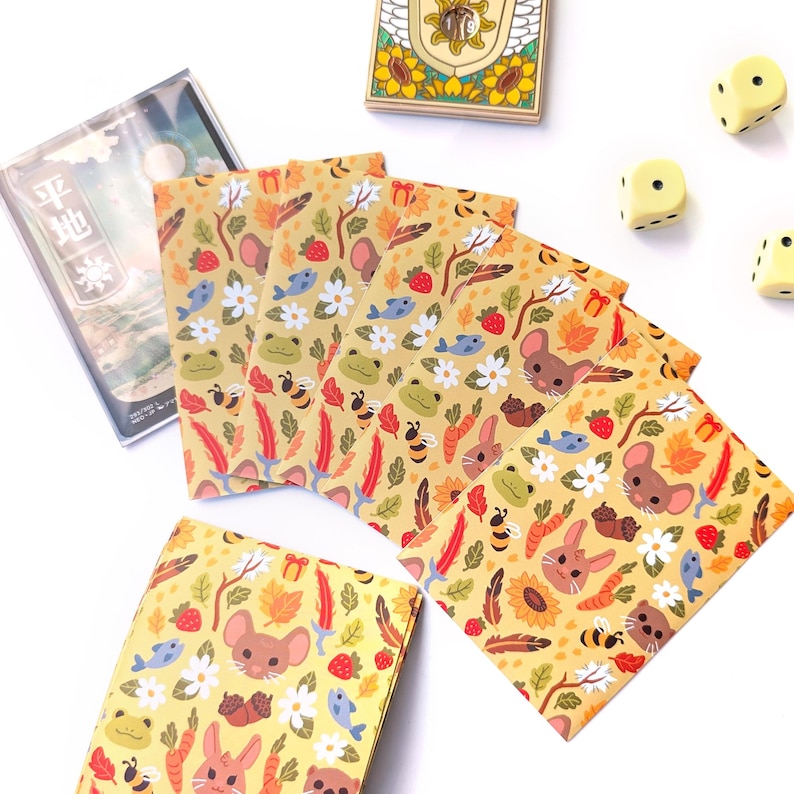 May include: A collection of illustrated stationery featuring a repeating pattern of woodland creatures, including mice, rabbits, bees, and fish, set against a yellow background. Additional items include dice, a wooden box, and a clear plastic case with Japanese text.