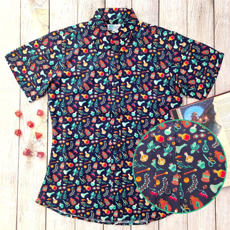 Puede incluir: Una camisa de botones de manga corta de color azul marino con un estampado colorido de frascos de pociones, hierbas y otros objetos m&aacute;gicos. La camisa tiene un cuello abotonado y un corte holgado.