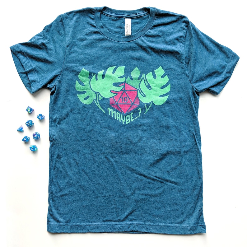 Puede incluir: Camiseta azul turquesa con un dise&ntilde;o de hojas de monstera verdes y un dado rojo de 10 caras con el texto "MAYBE...?"