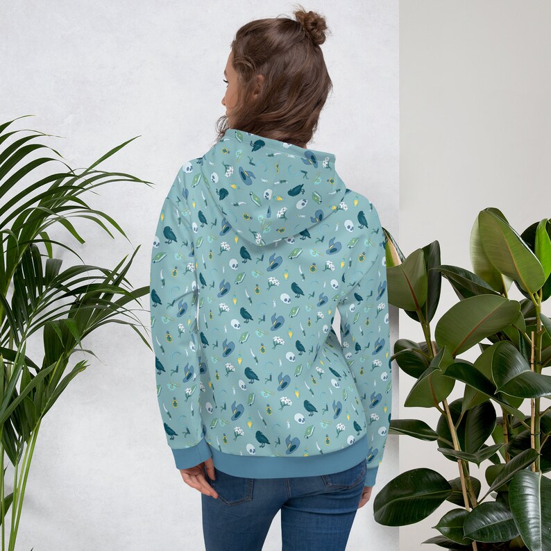 Puede incluir: Una sudadera con capucha azul claro con un patr&oacute;n de p&aacute;jaros, calaveras, flores y otros peque&ntilde;os detalles. La sudadera tiene una capucha con cord&oacute;n y un bolsillo canguro.