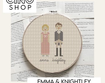May include: A cross stitch pattern featuring Emma and Knightley from the film Emma. The pattern is displayed in a white embroidery hoop with a beige background. The text "emma knightley" is stitched in black thread below the figures.