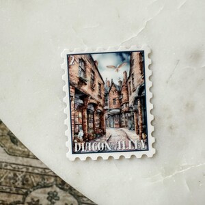 May include: A postage stamp featuring a detailed illustration of Diagon Alley, with cobblestone streets and brick buildings. The stamp has a white border and the text "DIAGON ALLEY". A white owl is visible in the image.